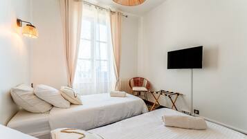 Quarto de hotel com duas camas, televisão, uma cadeira e um varal.