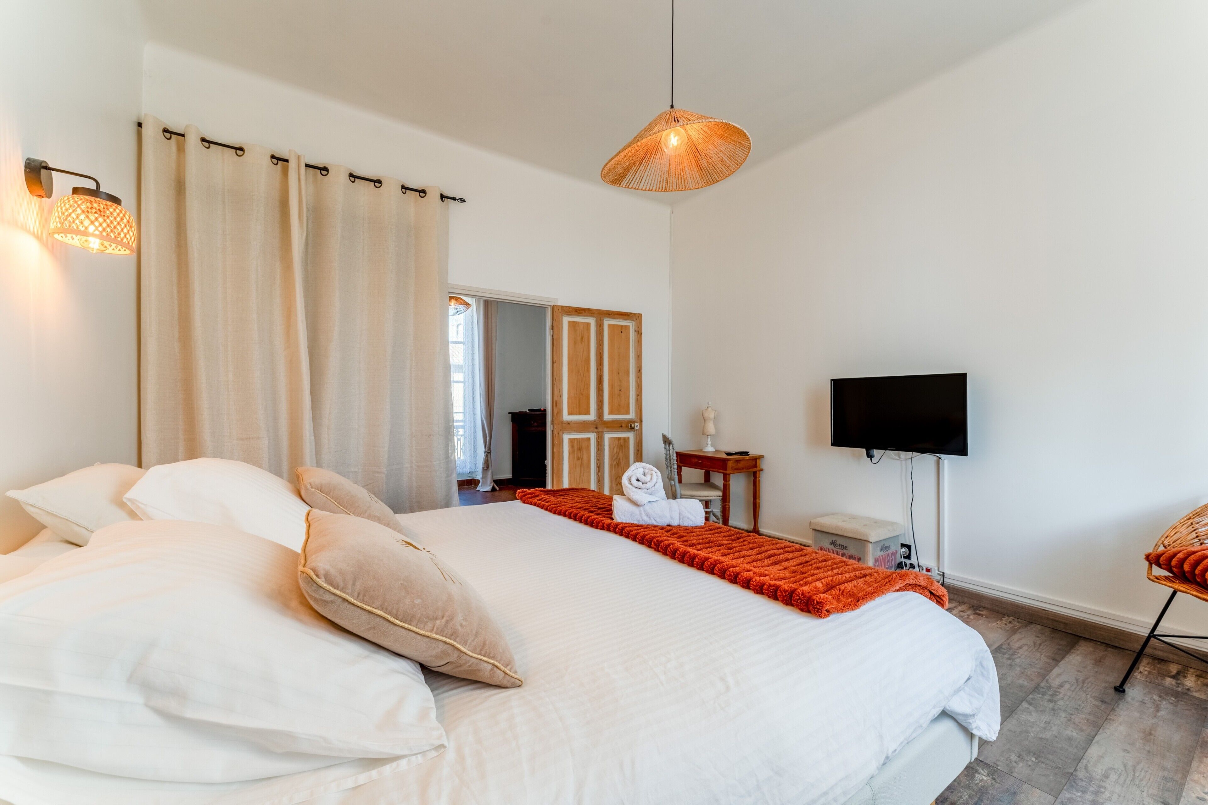 A bedroom with a large bed, a television, a chair, and a door leading to another room.