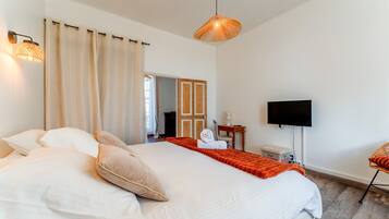 A bedroom with a large bed, a television, a chair, and a door leading to another room.