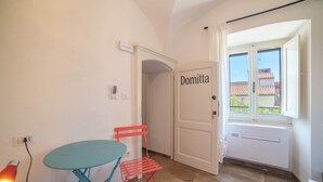 Habitació amb taula, cadira, radiador, una porta amb el nom 'Domitta' i finestra amb vistes.