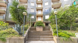 Un edificio residencial de varios pisos con una escalera central, balcones y abundante vegetación.
