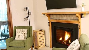 Ein Wohnzimmer mit Kamin, zwei grüne Sessel, einem Fernseher über dem Kamin und einer Stehlampe.