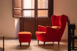 A red armchair and ottoman in a room with a wooden door and window. - Domo 24 (Bosa)