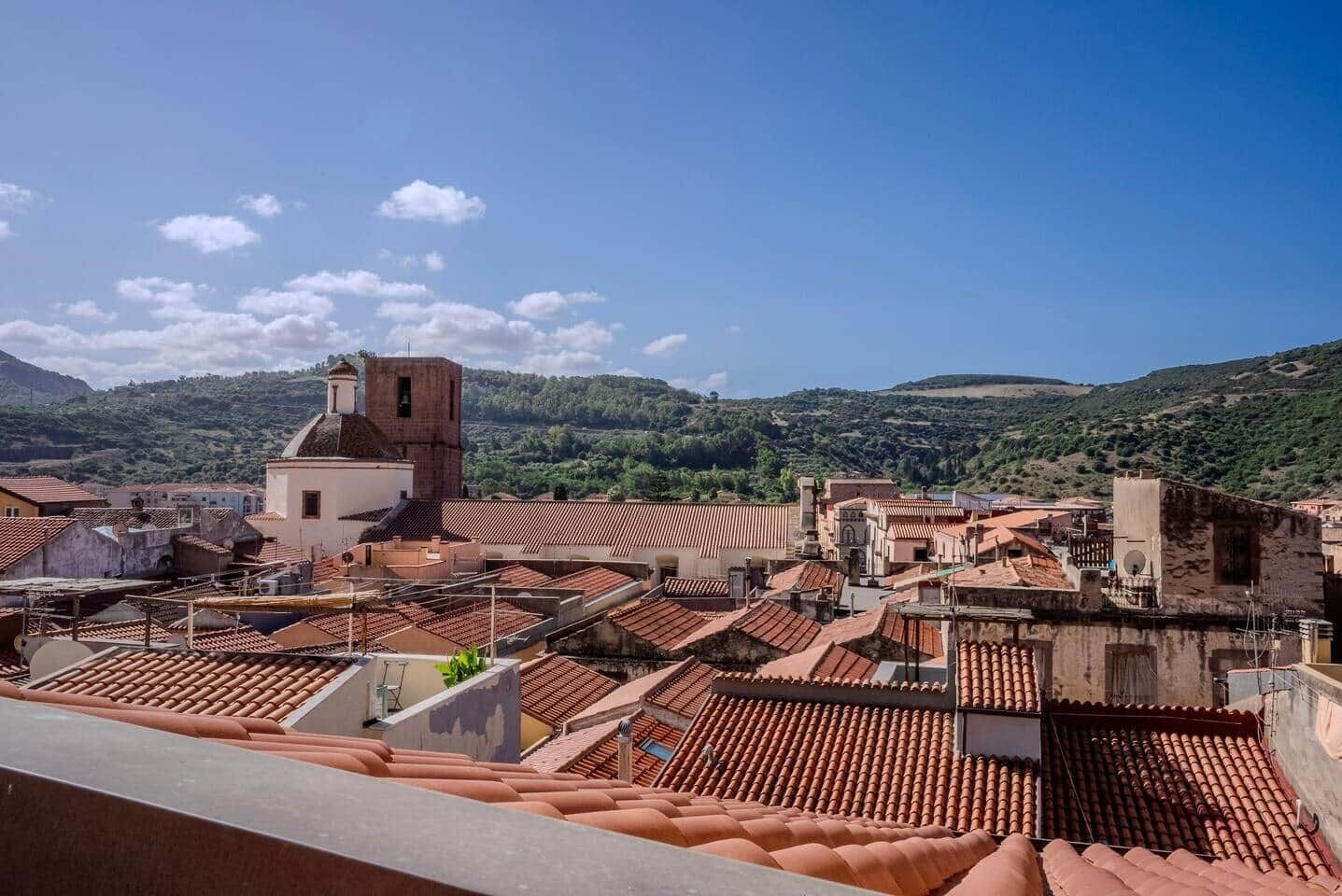 Une vue d’une ville avec des bâtiments aux toits de tuiles rouges et un imposant beffroi.