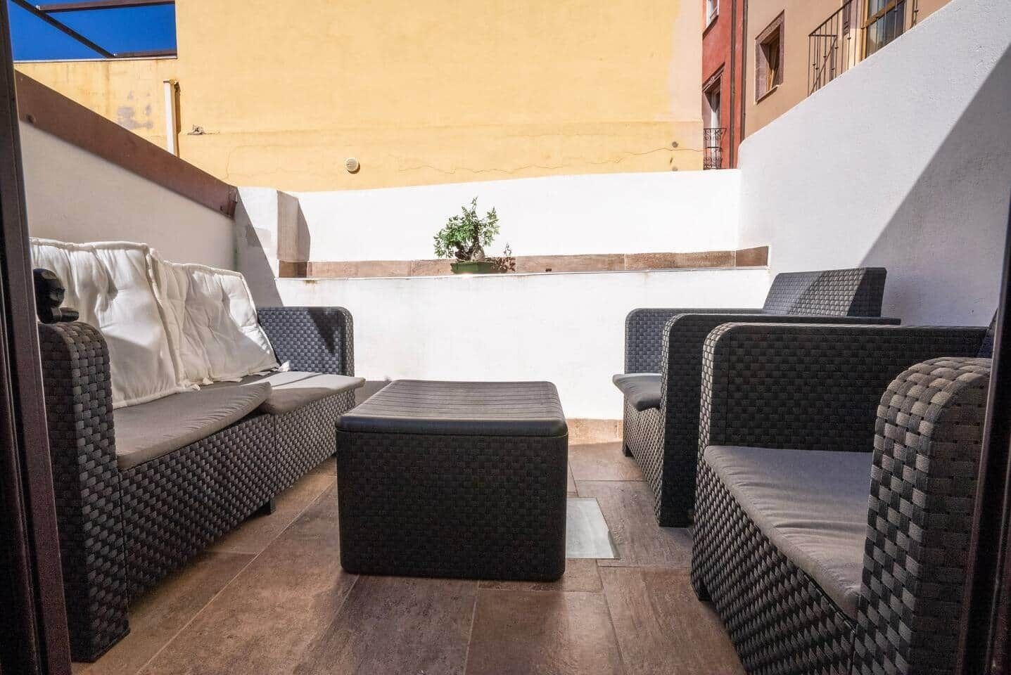 Un área de patio con muebles de mimbre, incluyendo un sofá y un reposapiés, y una pequeña planta en maceta.