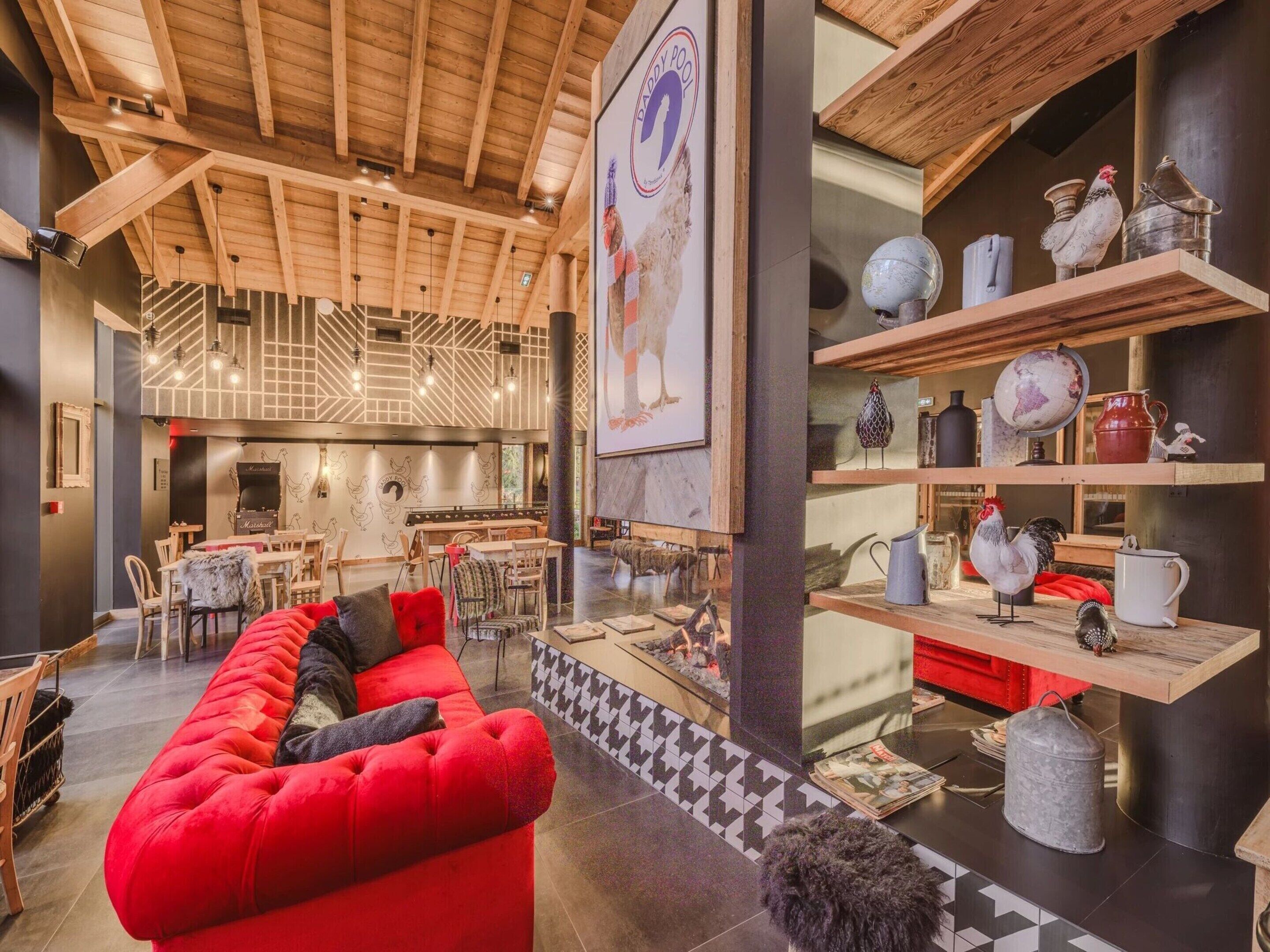 A cozy interior with a red sofa, wooden ceiling beams, and a dining area with tables and chairs.