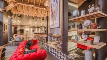 A cozy interior with a red sofa, wooden ceiling beams, and a dining area with tables and chairs.