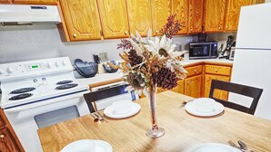 Una mesa de madera para comer con cuatro platos blancos y un jarrón de flores secas.