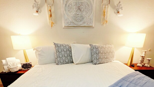 Una cama bien hecha con un edredón azul, dos lámparas de noche y apliques decorativos en la pared.