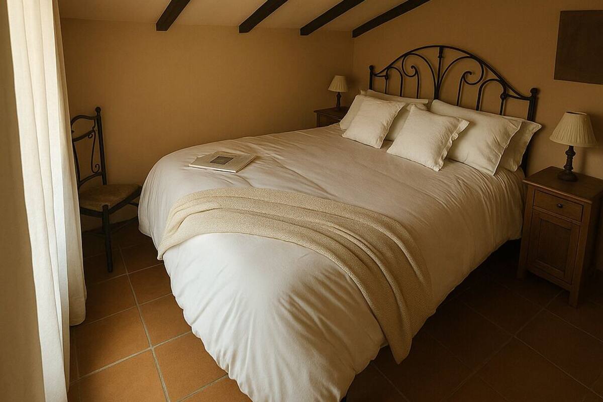 Un dormitorio con cama, mesitas de noche, una silla y una ventana con cortinas.