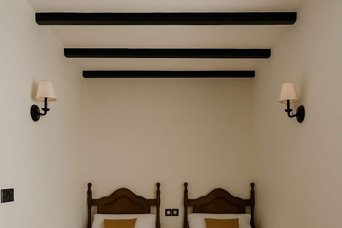 Una habitación con dos camas, cada una con cabeceros de madera y ropa de cama blanca. Hay lámparas de pared a cada lado de las camas.