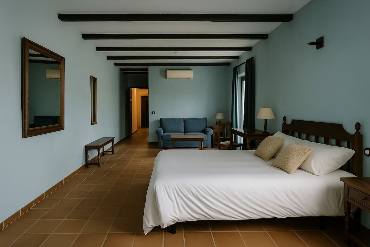 Una habitación de hotel con una cama grande, un sillón azul, una mesita pequeña y una mesita de noche.