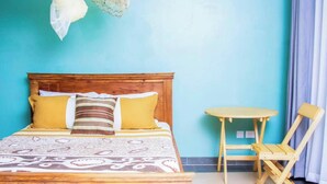 Une chambre à coucher avec un lit en bois, deux oreillers, une couvre-lit à motifs, une petite table ronde et une chaise pliante.