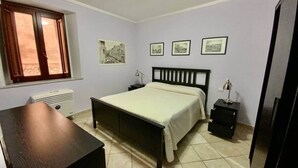 Ein Schlafzimmer mit Bett, Nachttischen, einem Schreibtisch, einem Fenster und Bildern an der Wand.