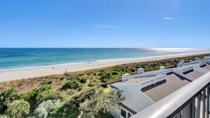 Blick auf einen Strand vom Balkon aus, mit blauem Himmel, Sandstrand und ein paar Personen in der Ferne.