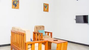 Een kamer met een houten bank en fauteuil, een kleine houten tafel en een aan de muur bevestigde televisie.