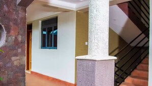A hallway with a white column, a window with blue frames, and a staircase with a black railing. - 10 - Family room at Mufasha Boutique And Suites (Kisoro)