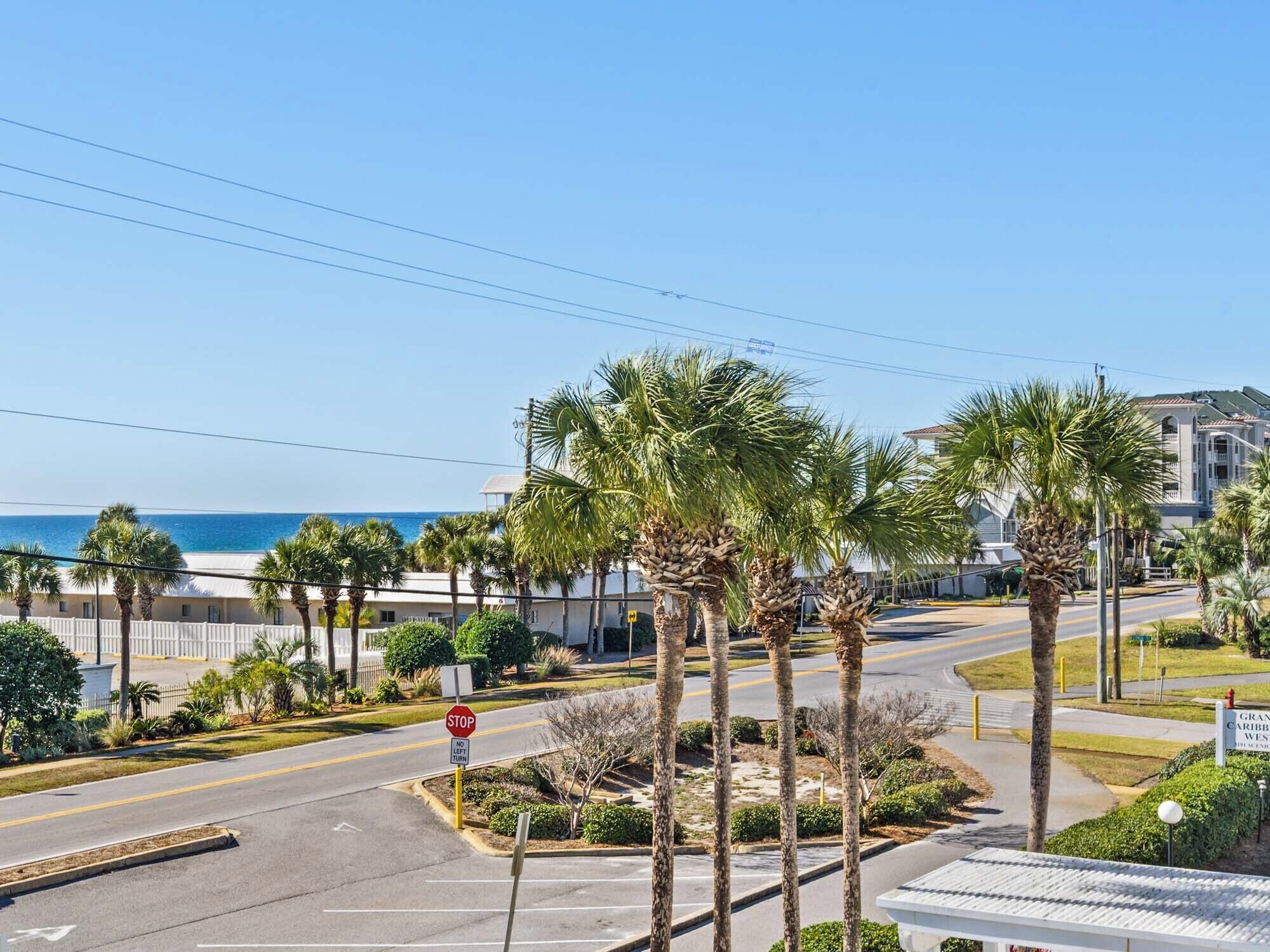 Una intersección costera con palmeras, una señal de parada y un edificio identificado como 'GRAND CARIFF BEACH WEST'.
