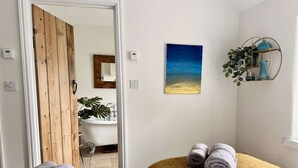 A room with two beds, a wooden door, a bathroom with a sink and mirror, a painting, and a plant on a shelf. - Wild Strawberry Cottage is a charming hideaway within a peaceful courtyard (Burnham Market, Norfolk)