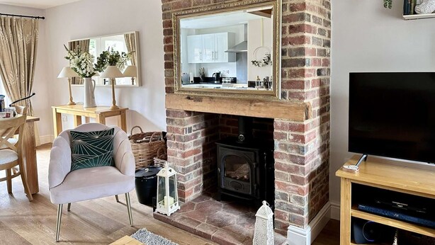 A living room with a brick fireplace, a television, and a dining area with a table and chairs. - Wild Strawberry Cottage is a charming hideaway within a peaceful courtyard (Burnham Market, Norfolk)