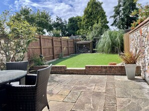 A patio area with a stone floor, wicker furniture, a small lawn, and a wooden fence. - Wild Strawberry Cottage is a charming hideaway within a peaceful courtyard (Burnham Market, Norfolk)