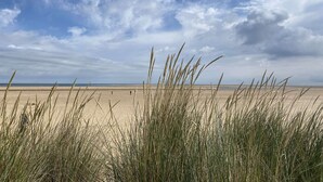 A beach with tall grass in the foreground and a clear sky with clouds. - Wild Strawberry Cottage is a charming hideaway within a peaceful courtyard (Burnham Market, Norfolk)
