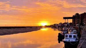 A harbor at sunset with boats docked along the quay, buildings in the background, and calm water reflecting the sky. - Traditional flint cottage, tucked away in the town of Wells-next-the-Sea (Wells-next-the-Sea)