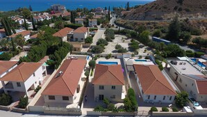 A coastal residential area with houses featuring red-tiled roofs, a central paved area, and a view of the sea.