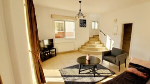A living room with a TV, a sofa, a coffee table, and a staircase leading to an upper floor.