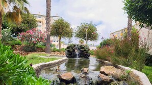 Ein angelegter Garten mit einem kleinen Wasserfall, umgeben von üppigem Grün und blühenden Pflanzen.
