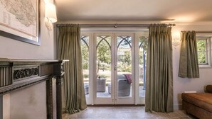A room with a fireplace, a stone floor, a sofa, and a view through a glass door to an outdoor area. - Charming Grade II listed sanctuary tucked away in Wells-next-the-Sea (Wells-next-the-Sea,)