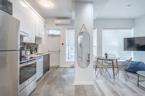 Eine moderne Küche mit Edelstahlgeräten, ein Essbereich mit Korbstühlen und ein großer Spiegel an der Wand.