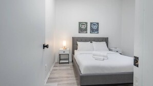 Une chambre d’hôtel moderne avec un lit soigneusement fait, une table de chevet avec une lampe et deux œuvres d’art accrochées au mur.