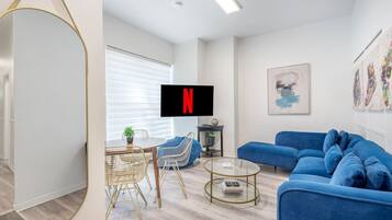 A modern living room with a blue sofa, a round coffee table, and a dining area with a small table and chairs.
