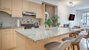 A modern kitchen with granite countertops, wooden cabinets, a built-in oven, and a central island with bar stools. - Charming Family Escape in Trendy Plateau Montreal (Montréal)