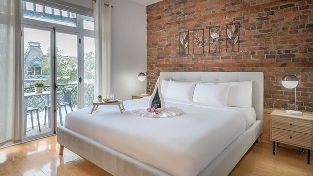 A modern bedroom with a large bed, a brick wall, and a balcony with a view. - Charming Family Escape in Trendy Plateau Montreal (Montréal)