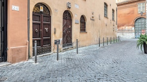 Eine Kopfsteinpflasterstraße mit historischen Gebäuden, Hausnummern und einem Maschendrahtzaun.