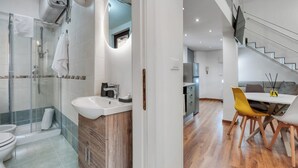 Ein modernes Badezimmer mit Glasdusche, Waschbecken und Toilette. Es gibt einen Essbereich mit Tisch und Stühlen.
