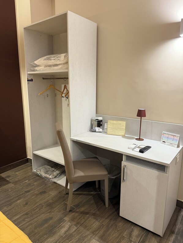 A compact hotel room with a desk, chair, and a small refrigerator. - B&B Leus Appartment (Reggio Calabria)