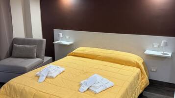Habitación de hotel con una cama amarilla, sofá gris y dos lámparas fijadas a la pared.