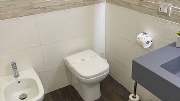 A bathroom with a bidet, toilet, sink, and a hairdryer on the wall.