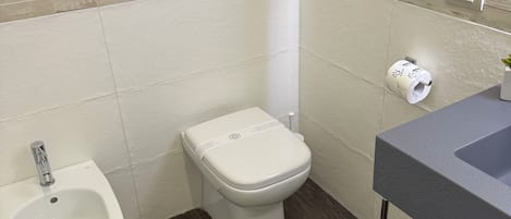 Ein Badezimmer mit Bidet, Toilette, Waschbecken und einem an der Wand befestigten Föhn.