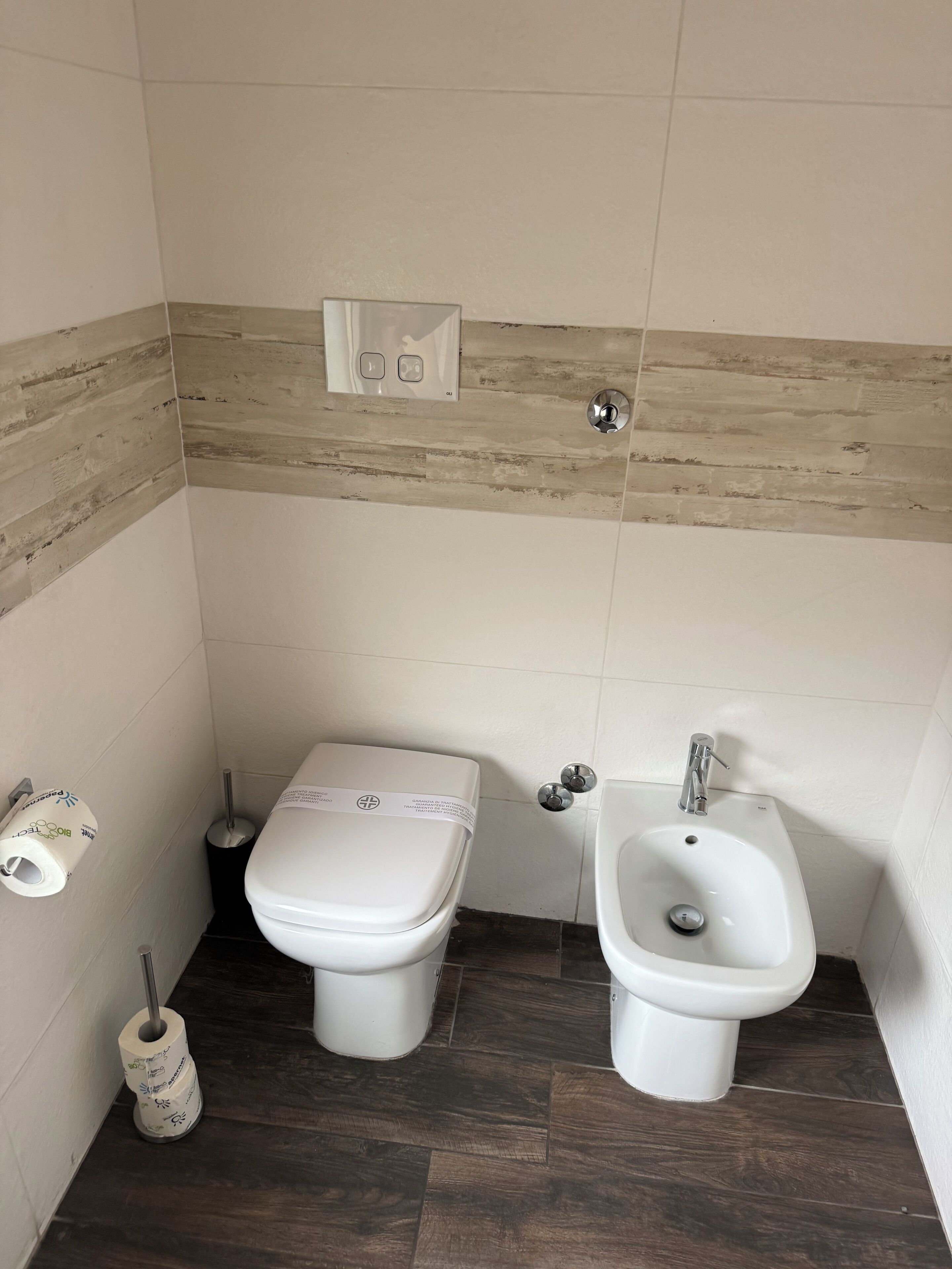 Ein kleines Badezimmer mit Toilette, Bidet und Toilettenpapierhalterung.