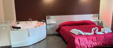A hotel room with a bed, a small desk, a chair, a bathtub, and a bench.