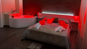 A modern bedroom with a large bed, a separate sitting area with a red-lit jacuzzi, and a nightstand with a lamp. - B&B Leus Appartment (Reggio Calabria)