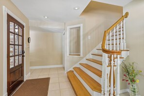 A staircase with wooden steps and white balusters, a brown doormat, and a door with glass panels. - 10 Gunnery Lane ~Heart of Sea Pines | Bike to Beach (Hilton Head Island)