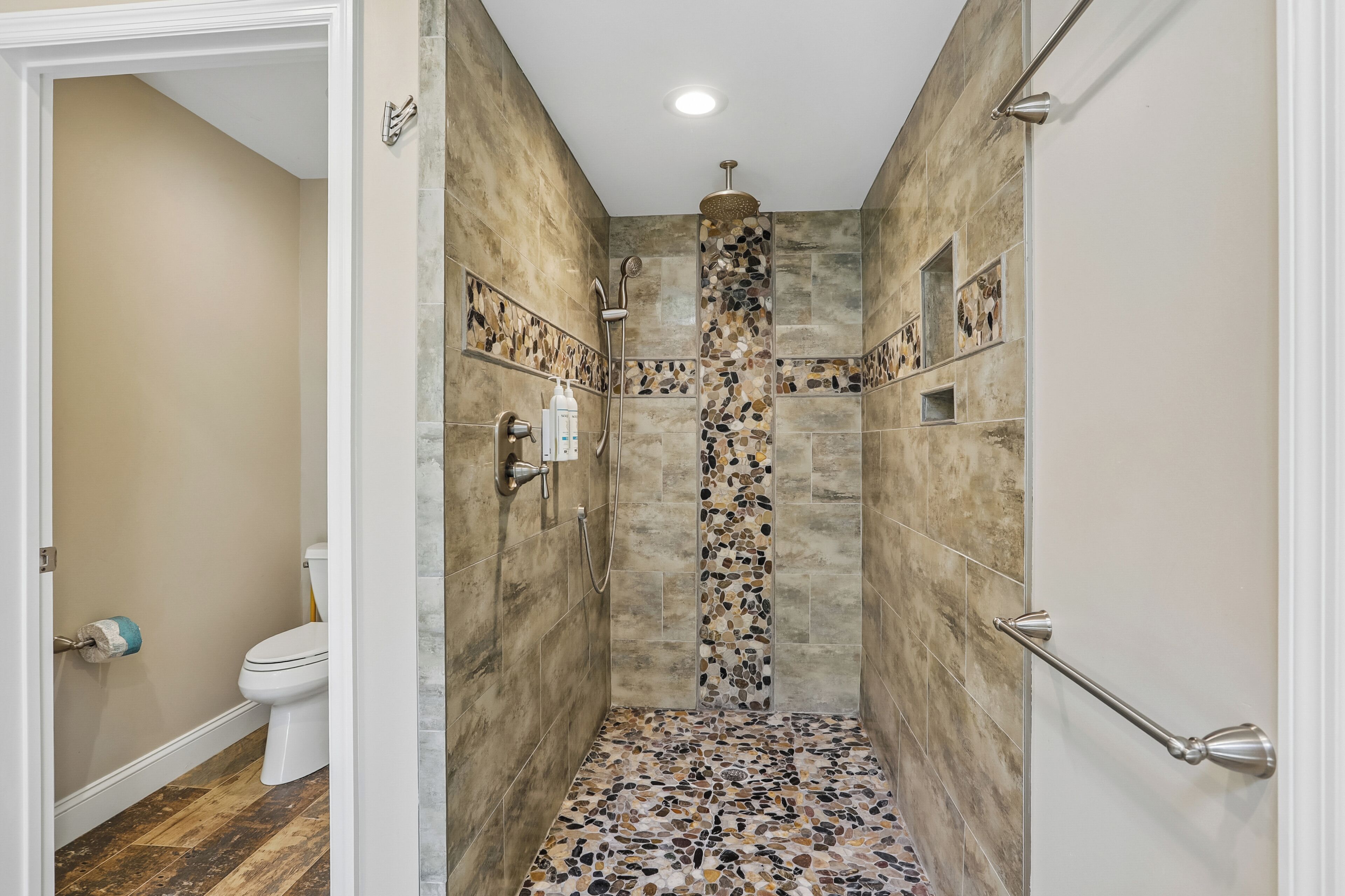 Ducha con pared de mosaico de piedra, inodoro y suelo de madera.