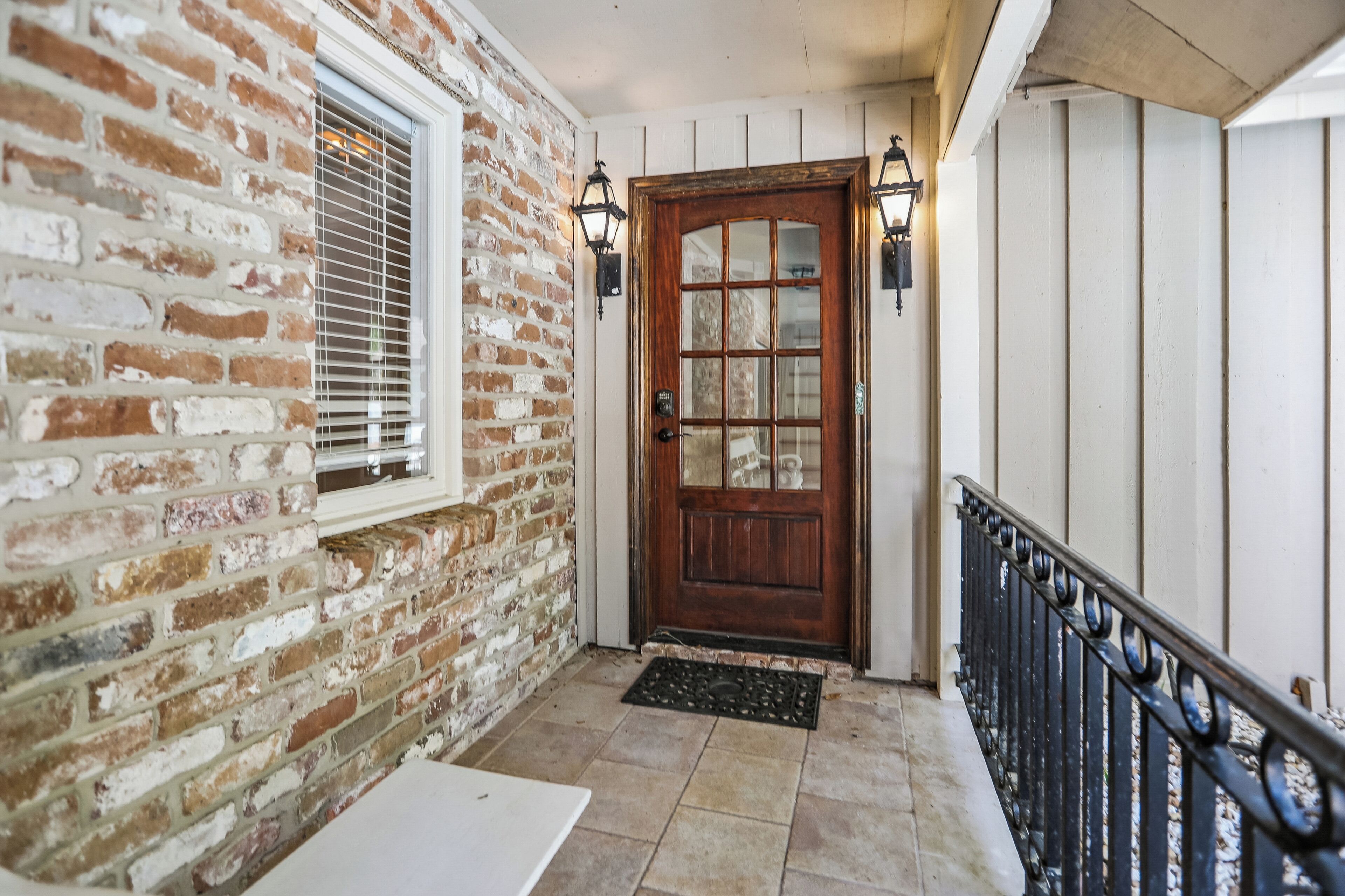 A brick exterior wall, a wooden door with glass panels, and a black metal railing.