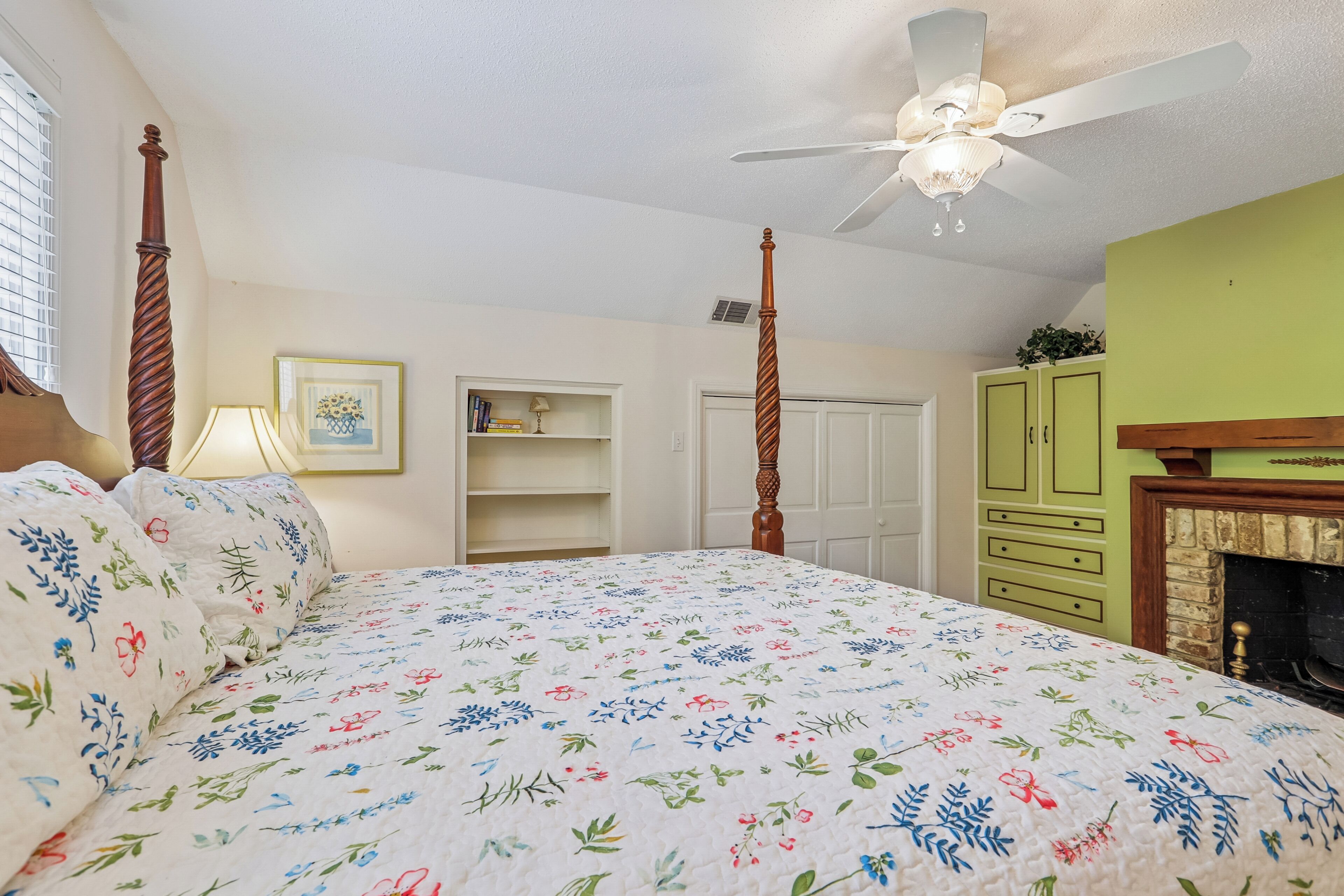 A bedroom with a four-poster bed, a ceiling fan, a fireplace, and a green wall.