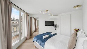 Hotelkamer met een groot bed, een televisie, een plafondventilator en uitzicht op de stad door grote ramen.